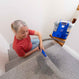 An older woman with gray hair tied back in a ponytail uses the Kleva Range KRAPOF® Spot & Stain Portable Remover with BONUS Cleaning Solution on a carpeted staircase, placing it on the step above as she tackles tough stains.