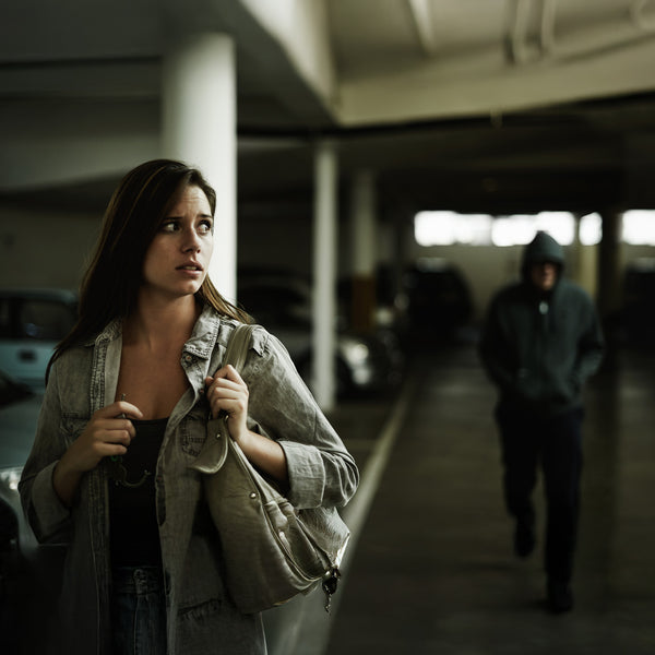 Woman sensing danger in parking lot followed by suspicious hooded man