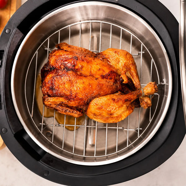 A whole roasted chicken with golden, crispy skin sits on a grill tray inside a stainless steel pressure cooker pot, shown from above, using the KLEVA® Spin Crisp Cooking Accessories Set by Kleva Range for perfect roasting results.