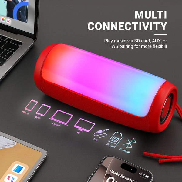 The Kleva® Glow Beats Speaker by Kleva Range, a red portable speaker with multicolored LED lights, sits on a black surface near a laptop and smartphone, showcasing Bluetooth, AUX, and SD card connectivity for crystal-clear sound.