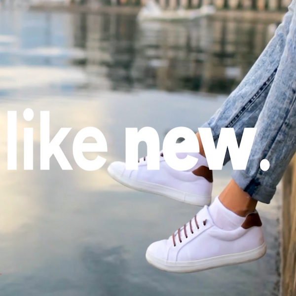 Wearing white sneakers with brown accents and blue jeans, a person sits by the water. "Like new." appears in bold—showing how Kleva Clean Sneaks Automatic Shoe Cleaner by Kleva Range keeps shoes looking fresh.