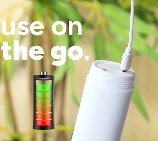The Kleva Range Clean Sneaks Automatic Shoe Cleaner, in white, is being charged with a white cable. “Use on the go” and a full battery icon appear on-screen. The background has blurred green leaves. Make old shoes look new!.