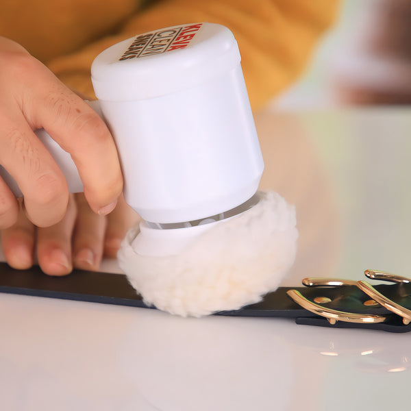 A hand uses the Kleva Range Kleva Clean Sneaks Automatic Shoe Cleaner with a fluffy pad to clean a black leather belt with a gold buckle on a white surface.