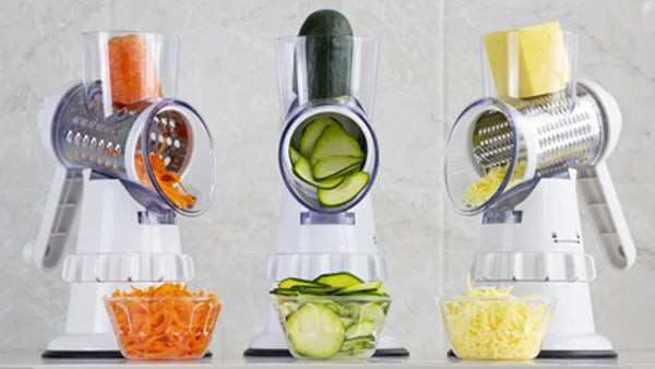 Three white Kleva Sumo Slicers with interchangeable drum blades grating carrots, slicing cucumbers, and shredding cheese into glass bowls.