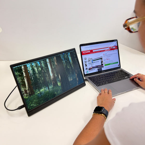 A person uses a Kleva Range Portable 15.6" Screen Extender as an external monitor, displaying a forest image, while their laptop shows a website; they're wearing glasses and a smartwatch.