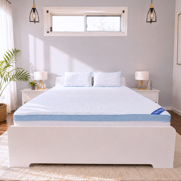 A neatly made bed featuring a white frame and the Super Sleeper Pro Straight 2 Sleep® Mattress Topper with Cooling Technology, along with two BONUS matching pillows, is centered in a bright bedroom with white walls, two nightstands, lamps, and a window above the bed.