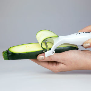A person uses a white vegetable peeler to slice zucchini beside the Kleva Range KlevaCut® Professional Chef 3pc Knife Set, which features Japanese steel, MRE sharpening technology, $130 in free gifts, and a lifetime guarantee.