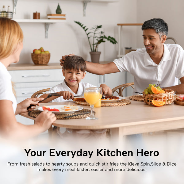 A family of three enjoys breakfast at the kitchen table with juice and fruit. Behind them, the Kleva® Spin, Slice & Dice from Kleva Range sits on the shelf—an all-in-one kitchen prep solution—alongside several baskets.