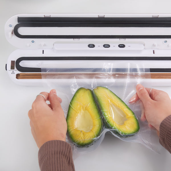 A person uses the Kleva® Vac Seal & Save Food Saver Vacuum Sealer by Kleva Range to seal two avocado halves in a clear bag, helping keep food fresh. The open machine is on a white surface, with free sealer bag rolls included.