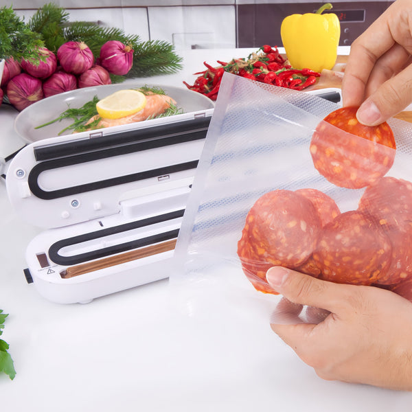 A person uses the Kleva® Vac Seal & Save Food Saver Vacuum Sealer from Kleva Range to seal cured meat slices in clear bags, keeping food fresh with vegetables and herbs visible on the kitchen counter. Includes FREE sealer bag rolls.