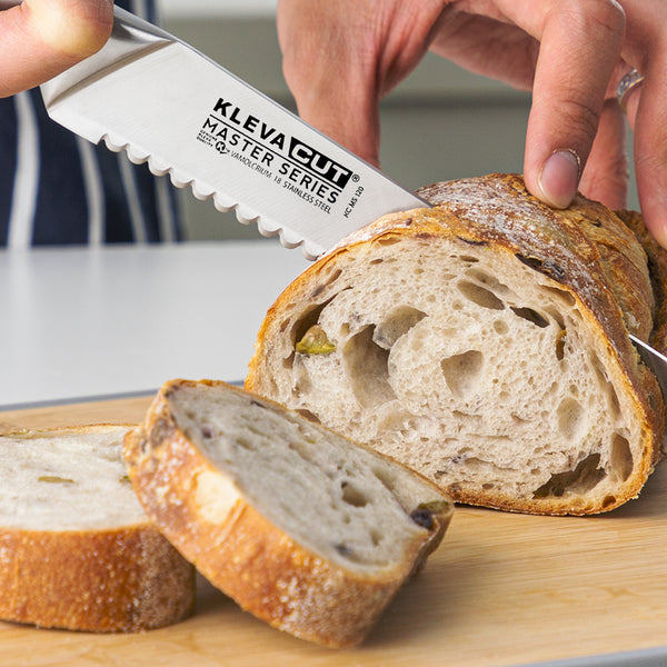 A person slices a rustic loaf with the Kleva Range KlevaCut® Master Series 20cm Double-Edge Serrated Bread Knife on a wooden cutting board; two slices are already cut.