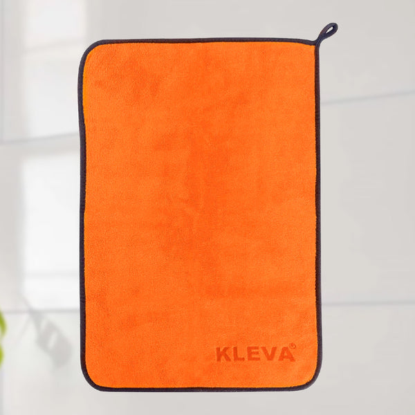 An orange rectangular Kleva Range The World's Best Cleaning Cloth with black trim and a small hanging loop is shown. "KLEVA" is embossed in the lower right corner. The microfibre cloth appears against a light, blurred background.