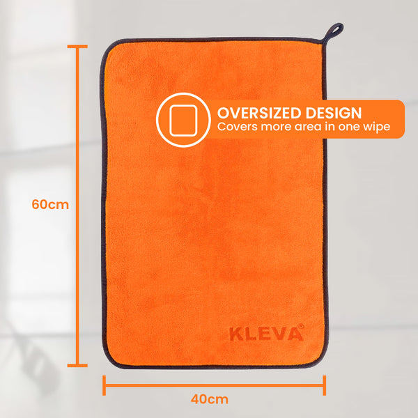 A bright orange rectangular microfibre cloth by Kleva Range, “The World's Best Cleaning Cloth,” with black edges (60x40cm) is displayed on a gray background. A label highlights its oversized design for faster cleaning.