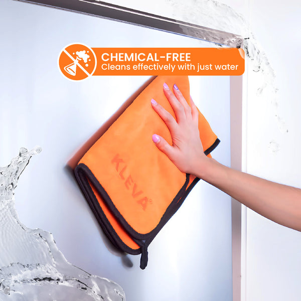A hand wipes glass with The World's Best Cleaning Cloth by Kleva Range—an orange reusable cloth. Water splashes nearby. Overlay: CHEMICAL-FREE Cleans effectively with just water.