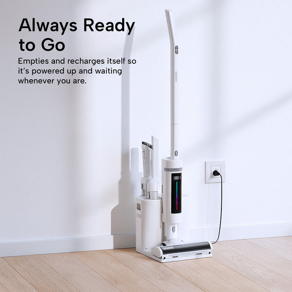 The KRAPOF® Compact Clean Self-Empty Cordless 2-in-1 Handy Vacuum Cleaner + Stick Vac by Kleva Range docks at its charging station on a light wood floor. Wall text highlights its self-emptying and self-recharging features.