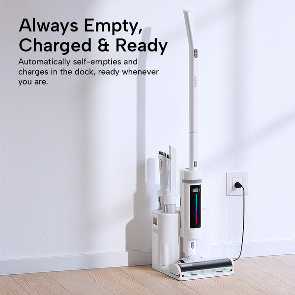 A white cordless floor cleaner and its matching charging dock stand against a white wall on a light wood floor. The product is shown with its power cord plugged into an outlet, and promotional text on the left reads 'Always Empty, Charged & Ready' with additional feature copy about self-emptying and charging.