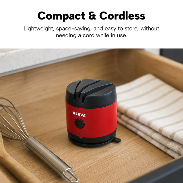 A red and black KLEVA® ElectraSharp – Advanced Electric Knife Sharpener from Kleva Range sits compactly in a wooden kitchen drawer beside a whisk and striped towel, highlighting its cordless, space-saving design and easy storage.