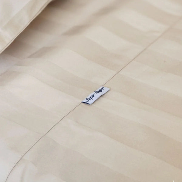A close-up of beige striped Imperial Dream Sheets™ 4pc Bedding Set by Super Sleeper Pro, crafted from 1200TC cotton sateen, with a small white Super Napper tag sewn onto the seam.