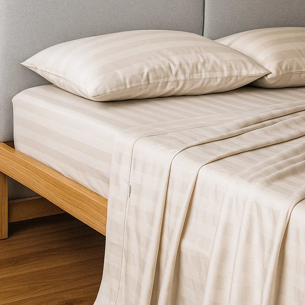 A neatly made bed features the Super Sleeper Pro Imperial Dream Sheets™ 4pc Bedding Set in beige stripes (1200TC cotton sateen) with two matching pillows, on a light wooden frame and gray upholstered headboard. Bedding drapes slightly over the sides.