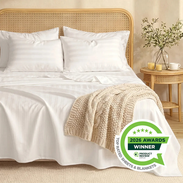A neatly made bed with Super Sleeper Pro's Imperial Dream Sheets™ 4pc Bedding Set, beige knit blanket at the foot, a round wooden nightstand with vase and glass. A 2026 Awards Winner badge appears in the bottom right corner.