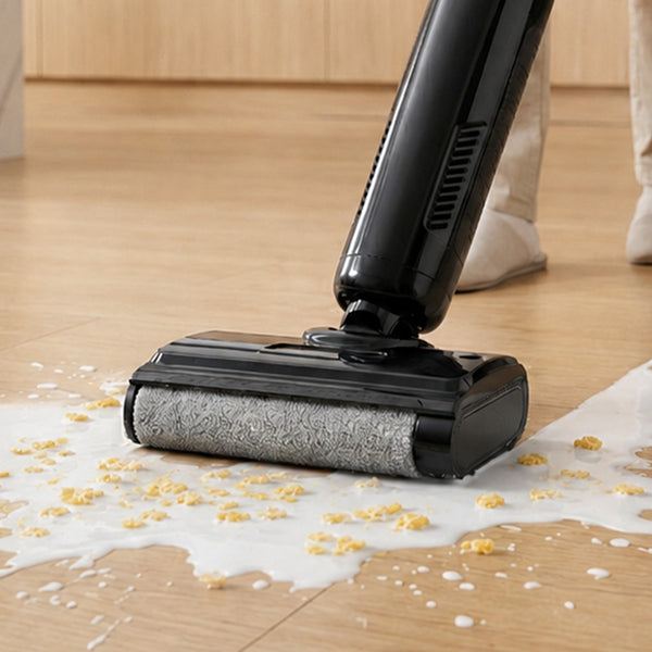 The Kleva Range FX5 Floor Washer - Roller Brush (Black) is cleaning spilled milk and cereal from a light wood floor, while a person wearing beige pants and boots stands in the background.
