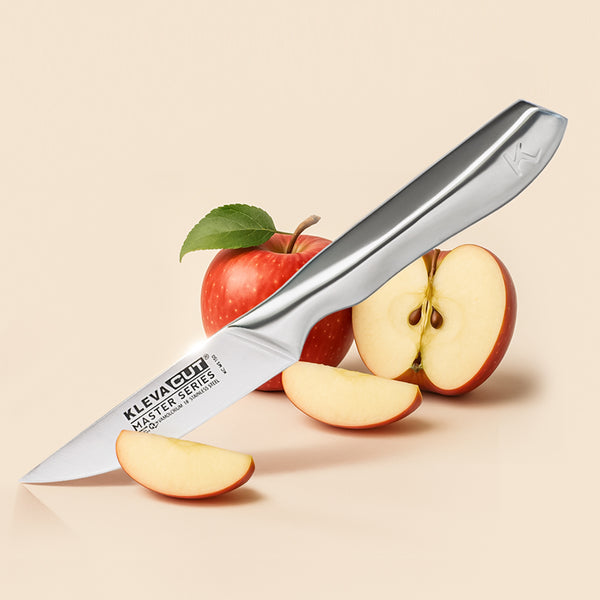 The KlevaCut® Master Series Professional Paring Knife - 9cm by Kleva Range rests on apple slices, with a whole red apple and a halved apple in the background on a light beige surface.