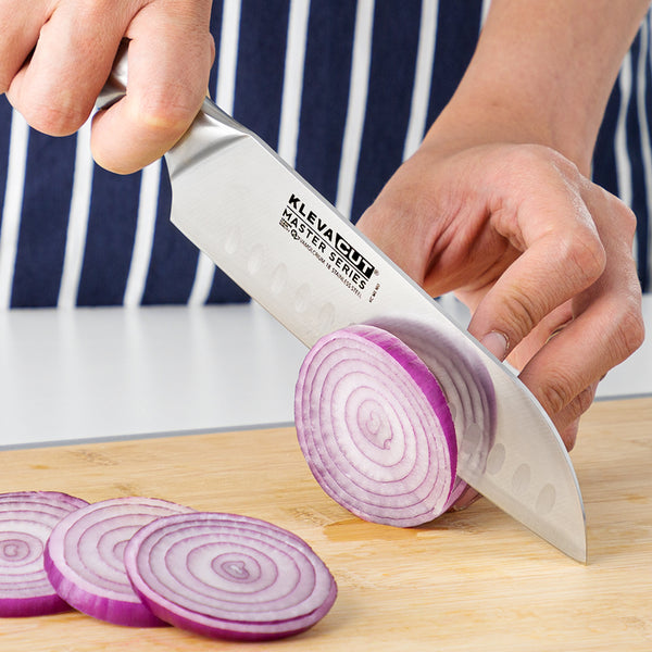 Wearing a striped apron, a person slices a red onion with the Kleva Range KlevaCut® Master Series Set 10pc Professional Chef Knife on a wooden board; several onion slices are already cut.