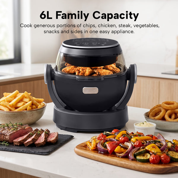 The Kleva® Spin Crisp IQ Rotating Digital Air Fryer by Kleva Range, in black with a transparent lid and 360° auto-rotate, sits on a kitchen counter filled with cooked chicken, surrounded by steak, fries, onion rings, veggies, dip. Text: 6L Family Capacity.