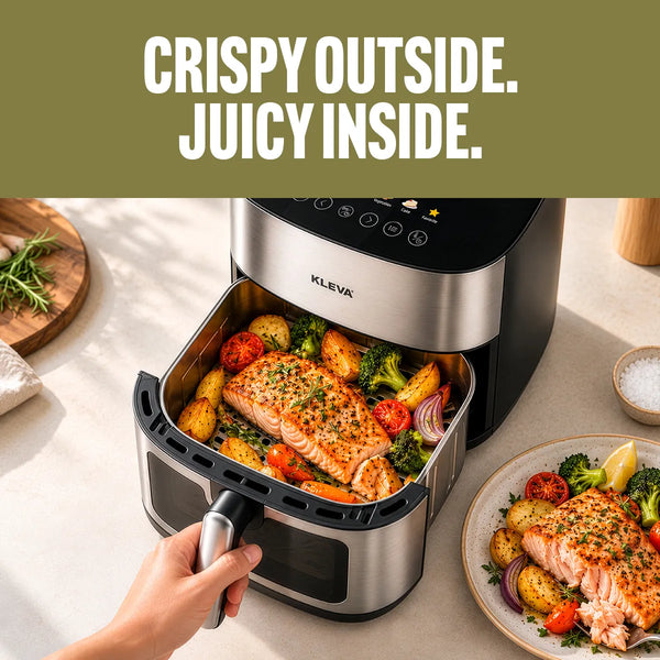 A KLEIVA air fryer sits on a light countertop with its basket open, showing cooked salmon and roasted vegetables inside. A hand is holding the handle, and a plate with food is visible at the lower right.