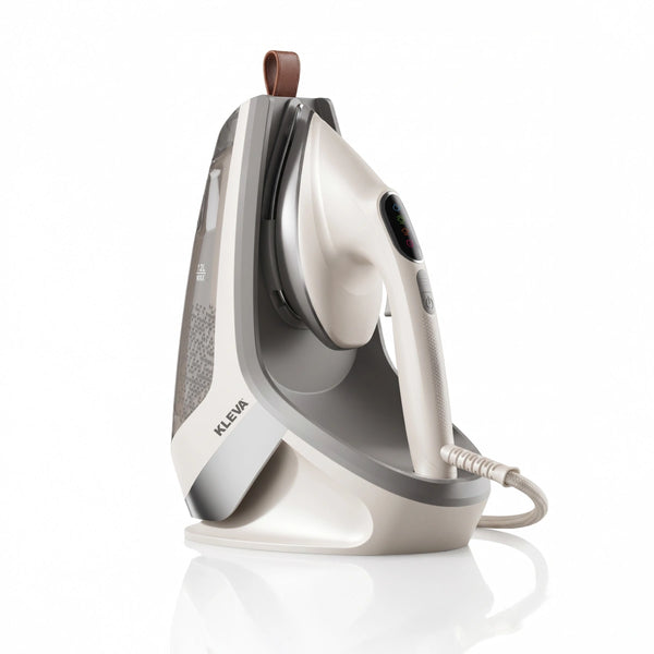The KLEVA® Crease Boss Steam Iron from Kleva Range is a white and gray electric steam iron featuring a clear water tank and an upright rest position on its base. Its visible power cord and convenient brown loop at the top make it easy to handle, while the brand name “Kleva Range” is displayed on the base. Designed as an effective wrinkle remover, this appliance offers the performance of a handheld garment steamer for efficient clothes care.