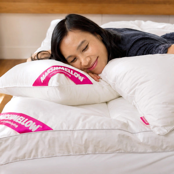 A woman with long dark hair relaxes, smiling with her eyes closed while resting on the Super Sleeper Pro Marshmellow™ Plush Mattress Topper and 2 free pillows, enjoying ultimate bed comfort.