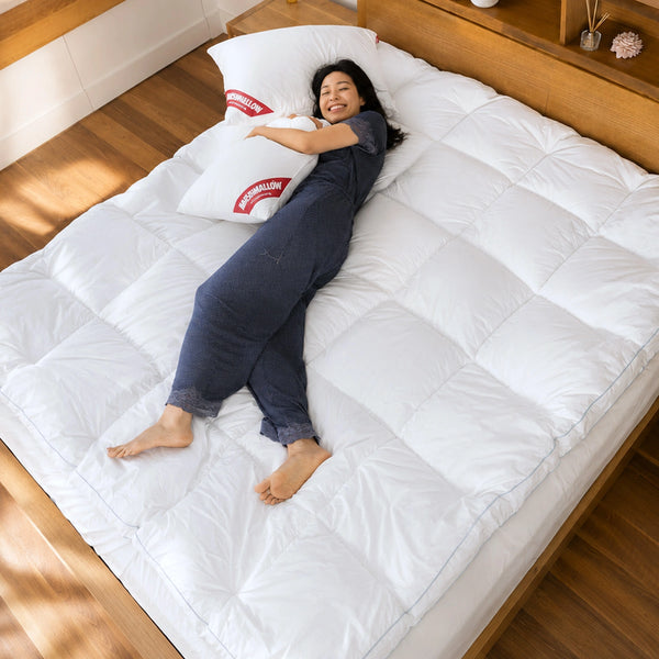 Relax in cozy comfort with the Super Sleeper Pro Marshmellow™ Plush Mattress Topper and two free pillows, shown here on a large bed with a white topper, wooden floors, headboard, and inviting décor for the perfect sleep sanctuary.