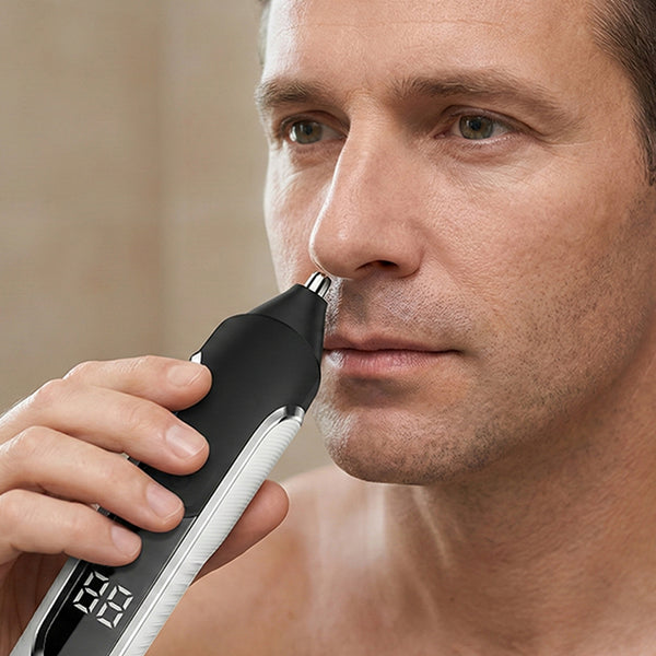 A man uses the KLEVA® TrimMaster 16-in-1 Multifunctional Premium Body and Beard Hair Trimmer by Kleva Range, holding the black and white cordless device with precision blades to his nostril; its digital screen is visible as he maintains a neutral expression.