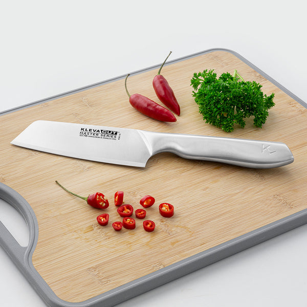 The Kleva Range KlevaCut® Master Series Professional Vegetable Knife - 14cm with an ergonomic handle is shown on a wooden cutting board with sliced red chili peppers, whole chilies, and fresh parsley in the background.