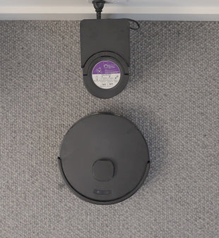 Looking down on the robot and its dock on grey loop-pile carpet.