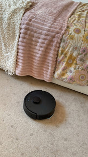 The robot crossing bedroom carpet at the foot of the bed.